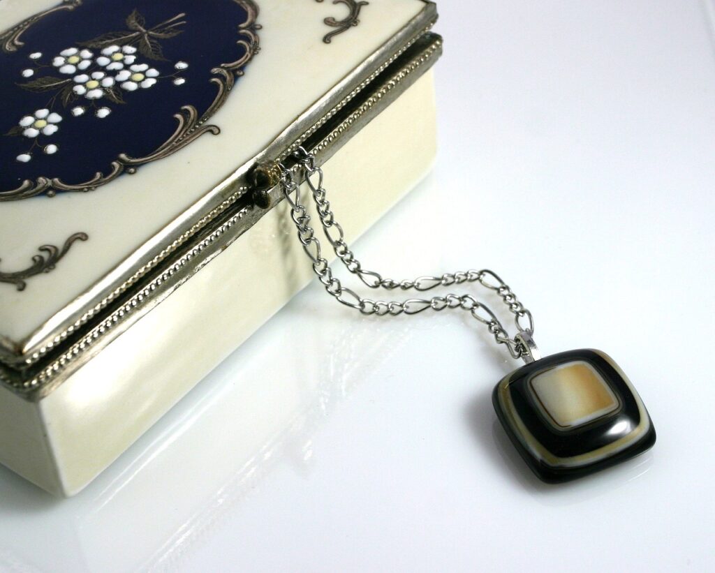 An elegant jewelry box with floral design and a silver locket on a chain draped over it.